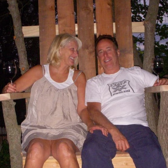Two people sitting on a wooden bench outdoors, holding wine glasses.